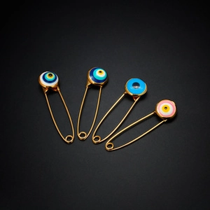 Detail of four golden metal pins with colorful evil eye charms on black background