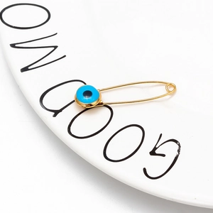 Close-up of golden evil eye brooch pin on a white ceramic plate with text