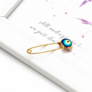 Detail of a golden evil eye pin charm displayed on a white textured frame background