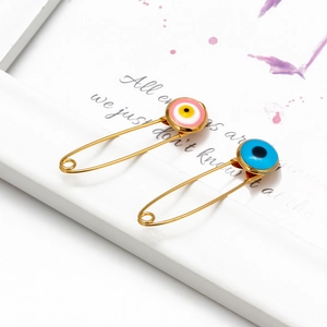 Detailed view of two gold evil eye pins with pink and blue enamel on a white frame