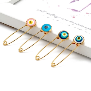 Detailed close-up of four gold evil eye brooches in pink, light blue, and navy blue shades