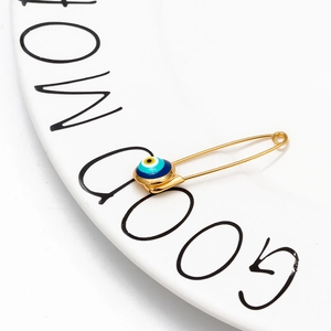 Macro shot of a golden safety pin featuring a blue evil eye charm on a white ceramic tray