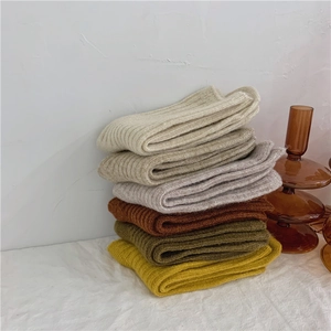 Stacked ribbed wool socks in neutral tones like beige and olive on a soft fabric