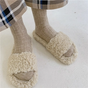 Close-up of beige plush slippers worn with warm wool socks for a cozy indoor look