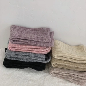 Close-up of thick wool socks in purple, pink, gray, and beige stacked on white cloth