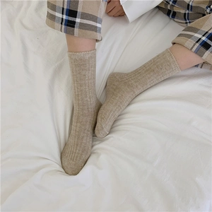 Close-up of thick beige wool blend ribbed socks worn by a model on a soft white duvet