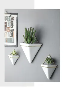 Detail of triangular white ceramic wall planters with gold metal frames and succulents