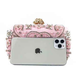 Detailed view of pink luxury beaded evening bag with pearls and rhinestones next to a phone