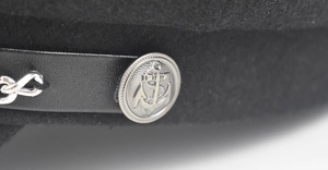 Detailed macro view of silver anchor embossed button and metal chain on black wool baker boy hat