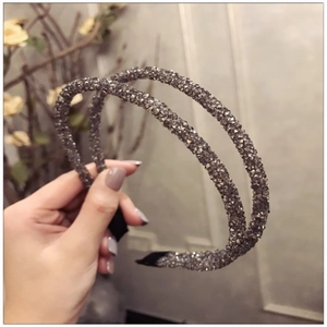 Close-up of hand holding two dark grey crystal-beaded headbands with sparkling details
