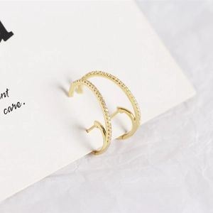 Macro shot of gold-plated paved diamond hoop earrings on white textured backdrop