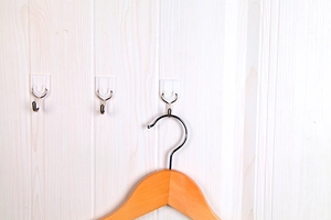 Three white adhesive wall hooks on wood panel with one holding a wooden clothes hanger