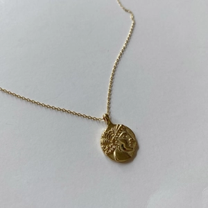 Close-up of golden coin pendant featuring vintage portrait relief on a delicate chain