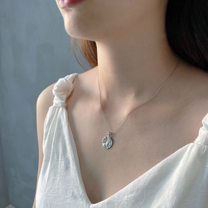 Detailed close-up of a silver irregular coin pendant necklace on a model wearing white lace