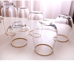 Detail view of six transparent egg-shaped glass cups with gold rims on a white desk