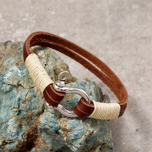 Detailed close-up of brown leather woven bracelet with silver horseshoe shackle buckle