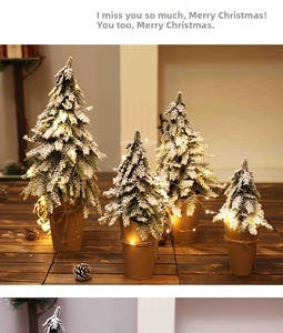 Detailed view of four mini flocked Christmas trees with warm LED lights and kraft paper pots