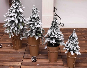 Set of four flocked mini Christmas trees in rustic kraft paper pots with jute twine