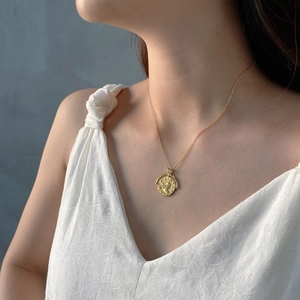 Close-up of a gold baroque coin pendant necklace featuring elegant vintage embossed texture