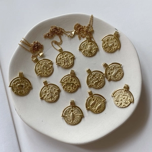 Detailed close-up of golden zodiac coin pendants displayed on a white ceramic plate