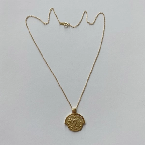 Detailed view of vintage gold coin pendant with embossed mythological wing figure carving