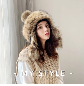 Brown faux fur trapper hat with fluffy pom-poms shown on a model for winter warmth