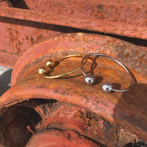 Polished gold and silver cuff bracelets with solid metal spheres on a textured background