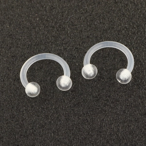 Detail of two transparent acrylic horseshoe piercings with screw balls on black surface
