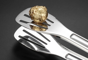 Détail macro d'une pince alimentaire en inox avec tête creuse saisissant une bille dorée