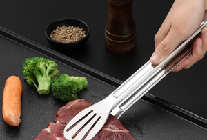 Vue rapprochée d'une pince de cuisine en inox saisissant de la viande en pleine cuisson