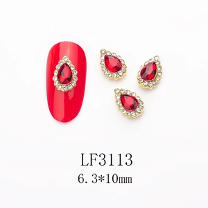 Macro detail of red pear-shaped nail charm with gold base and white crystal border