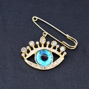 Macro view of gold safety pin brooch featuring a blue evil eye with sparkling crystals