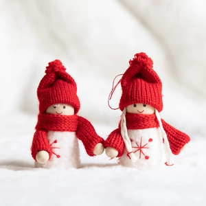 Handmade wooden Christmas dolls in red knit hats on soft white faux fur snow background
