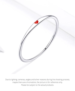 Dettaglio di un sottile anello in argento sterling 925 con un piccolo ciondolo a cuore rosso