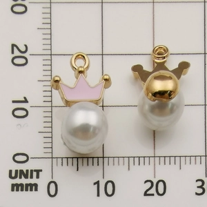 Macro view of two pink enamel crown pendants with white pearl on a mm grid ruler