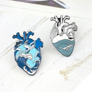 Detail of artistic enamel heart brooches with ocean wave patterns and whale silhouette