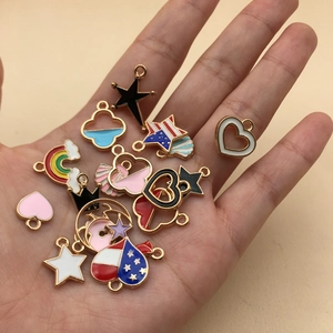 Assorted enamel jewelry charms with gold edging held in palm against beige background
