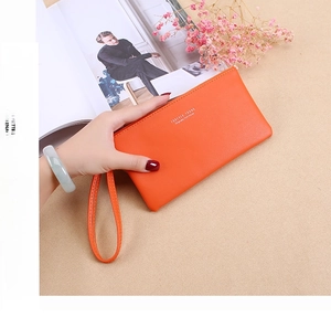 Detailed view of the bright orange leather wallet with wristlet strap and logo