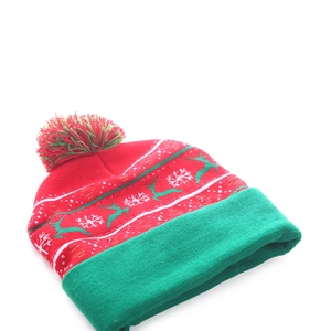 Detail of knitted Christmas beanie with white reindeer, snowflake patterns and a pom-pom