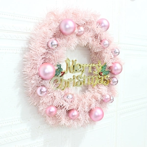 Pink Christmas wreath with glossy ornaments and gold Merry Christmas sign on white wall