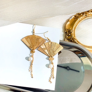 Detail of vintage gold fan earrings with delicate carvings, pearls and long tassels