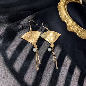 Detailed view of golden fan earrings with pearl tassels on black silk fabric