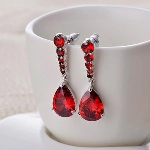 Close-up of long silver tassel earrings with pear-shaped red zircons hanging on a white cup