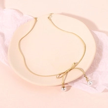 Detailed view of golden bowknot pearl necklace on a delicate snake chain accessory