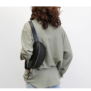 Detail van zwarte gewatteerde heuptas met brede riem gedragen als crossbodytas
