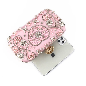 Pink satin clutch bag with pearls and floral clasp shown next to a smartphone