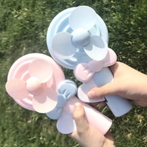 Pink and blue lollipop hand press fans displayed on a natural grass background