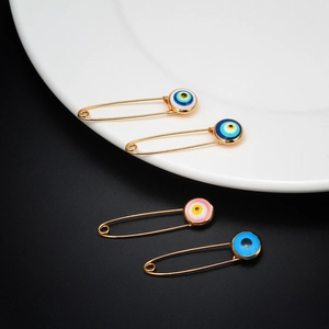 Detail of four gold-finish safety pins featuring colorful round evil eye charms on a tray