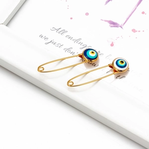 Close-up of golden evil eye safety pins with blue enamel detail on a decorative background