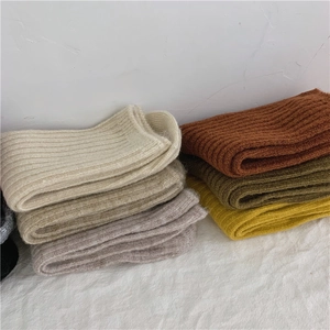 Close-up of stacked wool knit socks in beige, brown, and olive with detailed textures